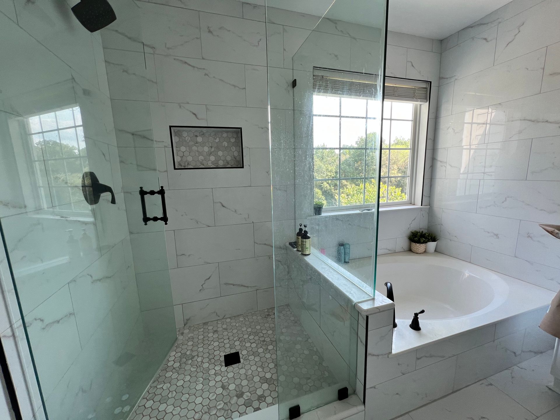 Modern bathroom with white marble tile, glass shower, and a tub.
