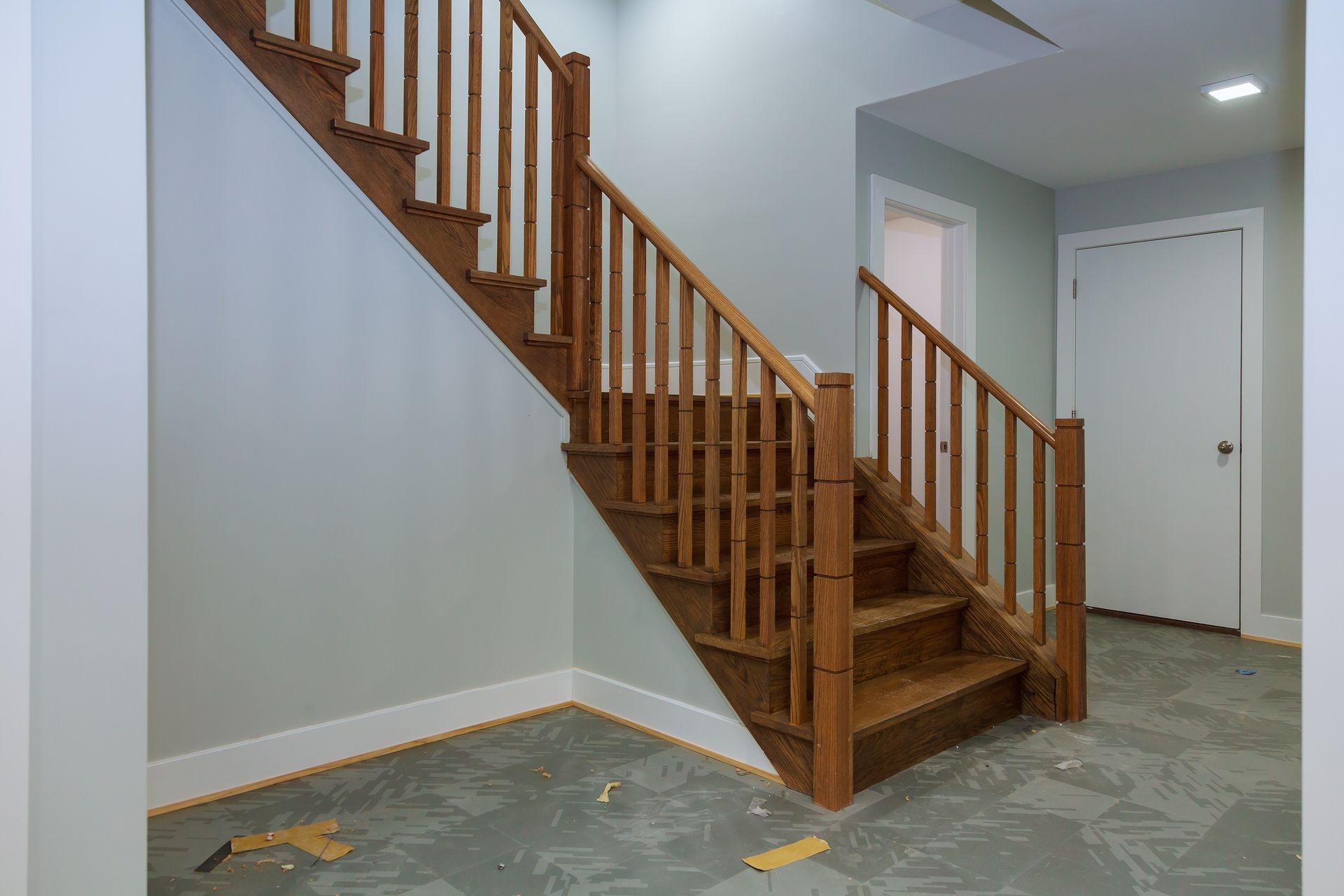 Wooden staircase with railings in a light-colored room with white trim.
