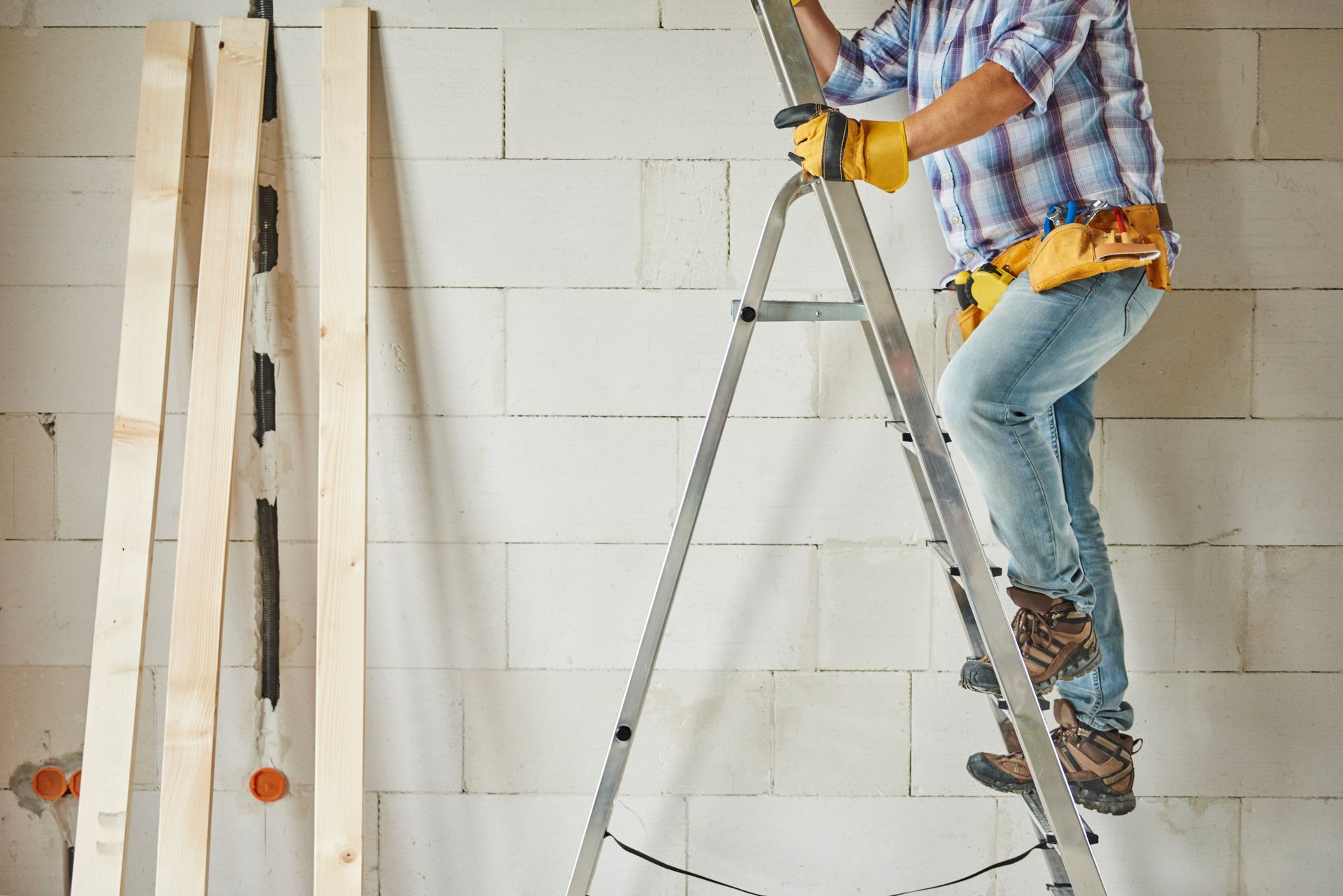 A man is standing on a ladder in front of a brick wall.