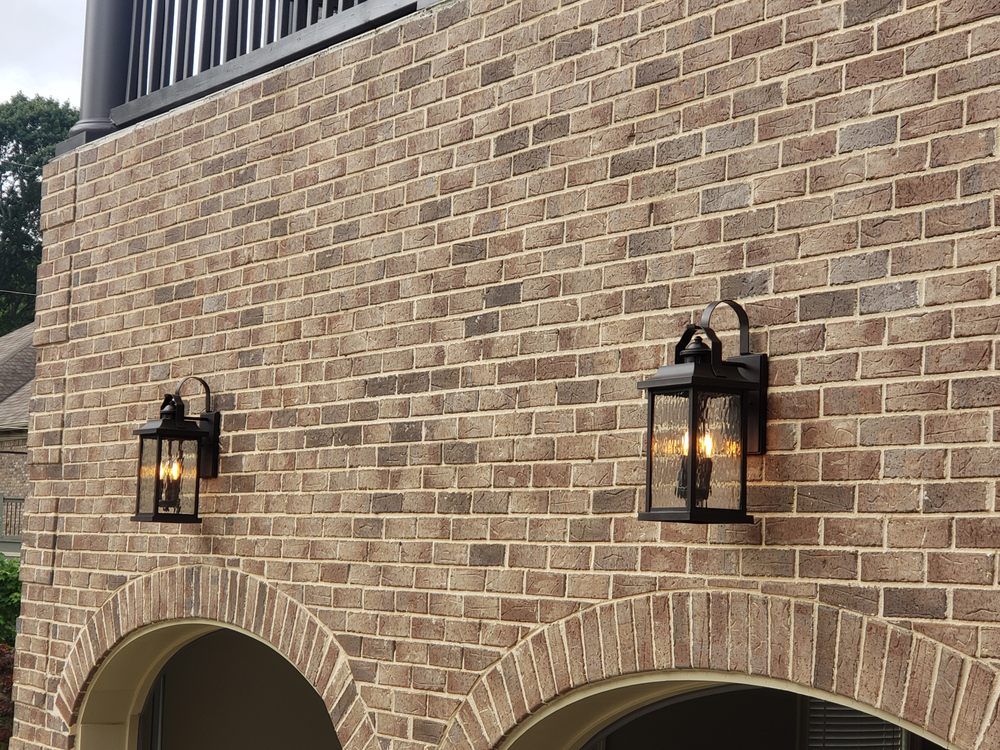 Two lanterns are hanging on the side of a brick building.