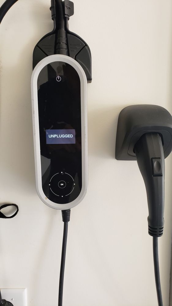 A charger is hanging on a wall next to a plug.