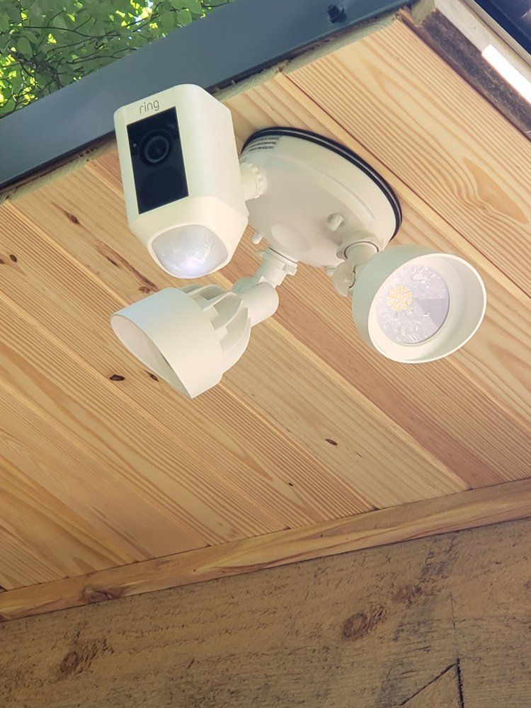 A flood light camera is mounted to the ceiling of a wooden building.