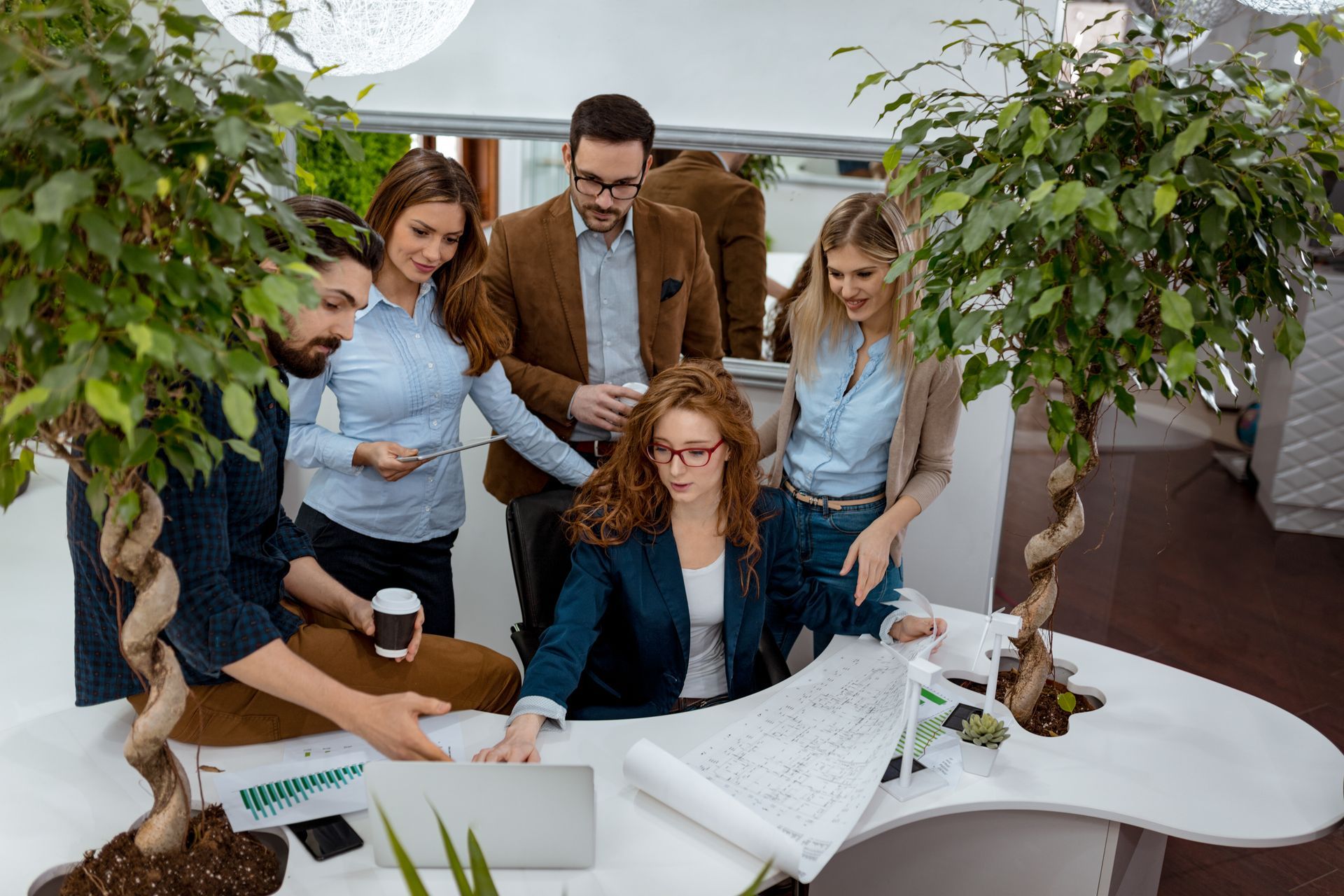 Group of people reviewing documents around a white table in a bright office or greenhouse setting