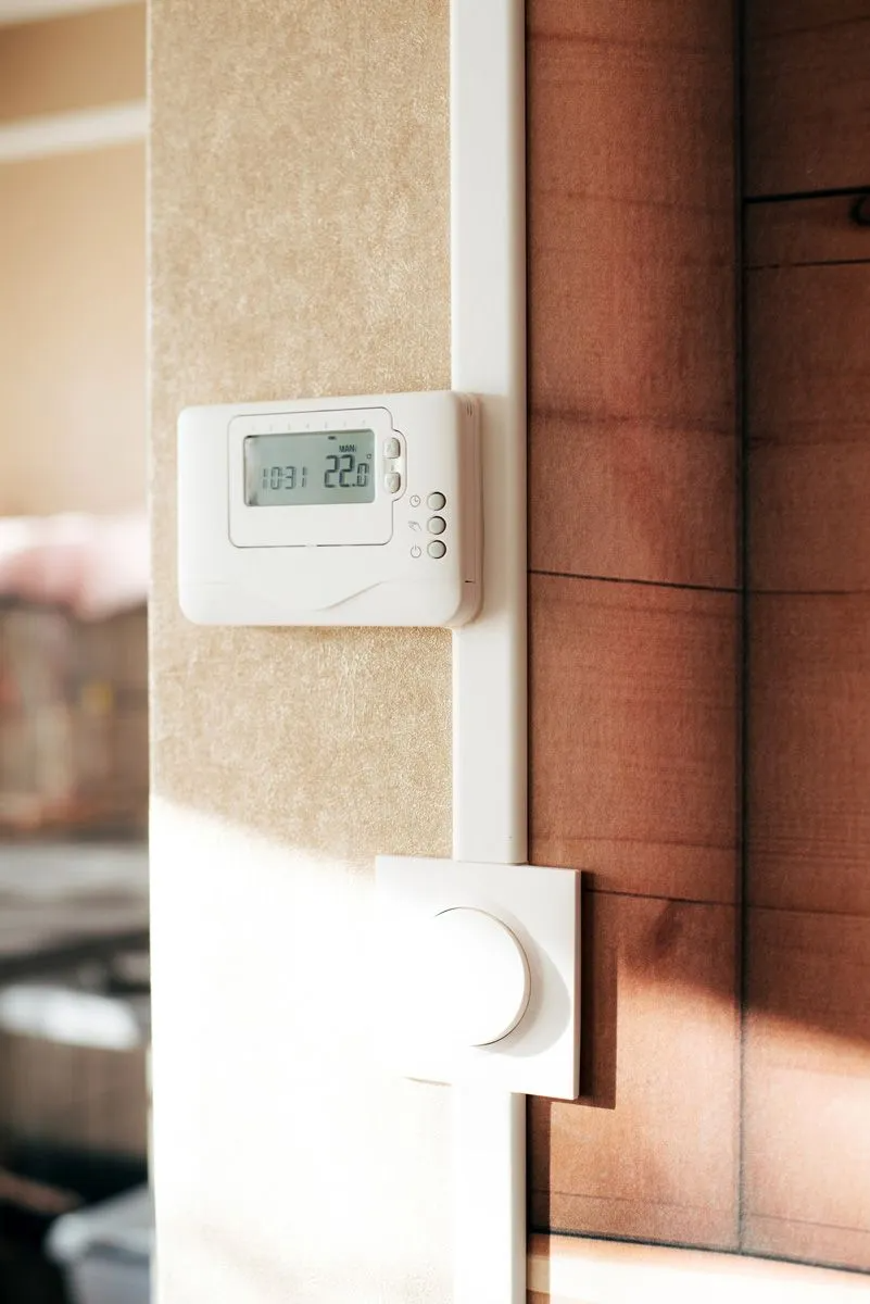 A thermostat is hanging on a wall next to a light switch.