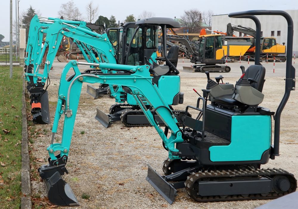 A Row Of Small Excavators Are Parked In A Gravel Lot — Red Shed Hire In Wauchope, NSW