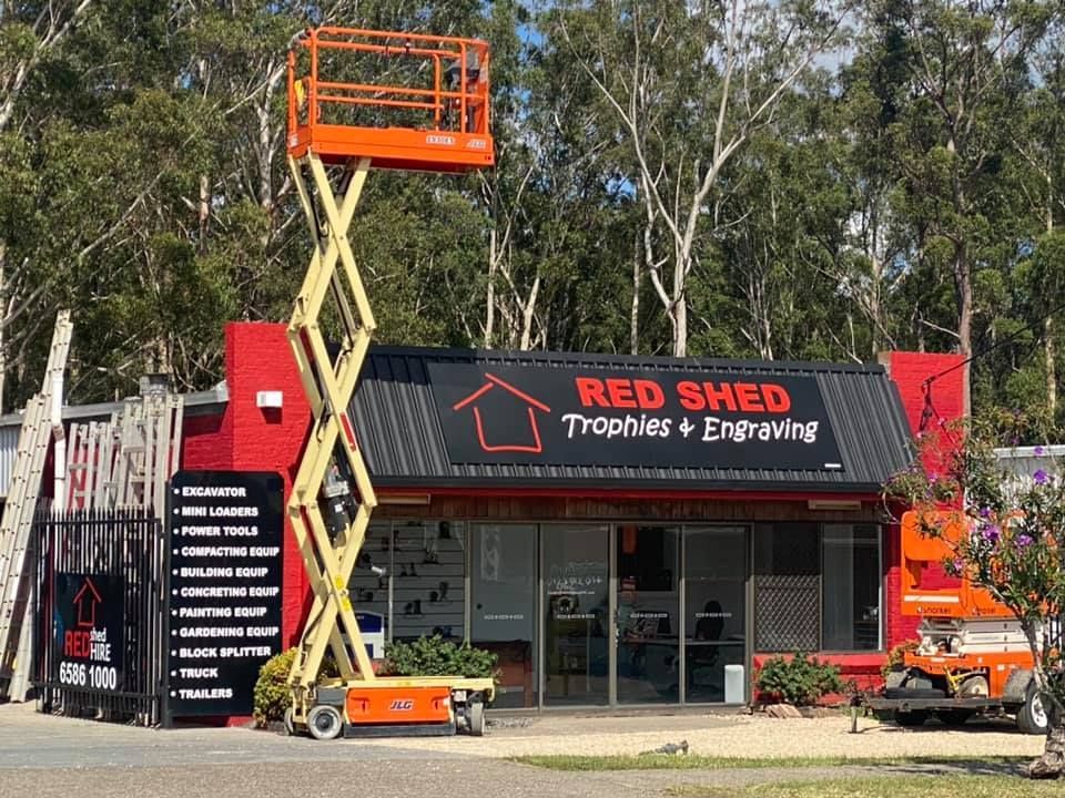 A Scissor Lift Is Sitting In Front Of A Red Shed Trophy And Engraving Store — Red Shed Hire In Wauchope, NSW