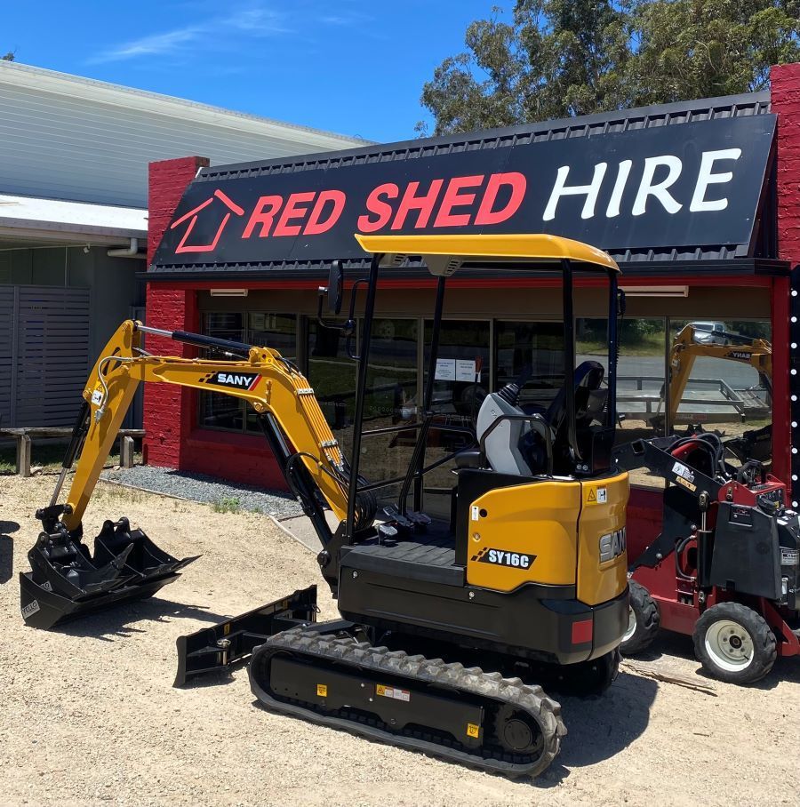 A Yellow Excavator is Parked in Front of a Red Shed Hire Store — Red Shed Hire In Wauchope, NSW
