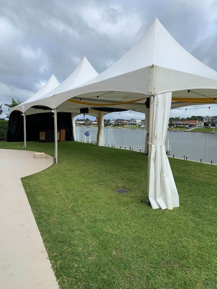 A white tent is sitting on top of a lush green field next to a body of water — Red Shed Hire In Port Macquarie, NSW