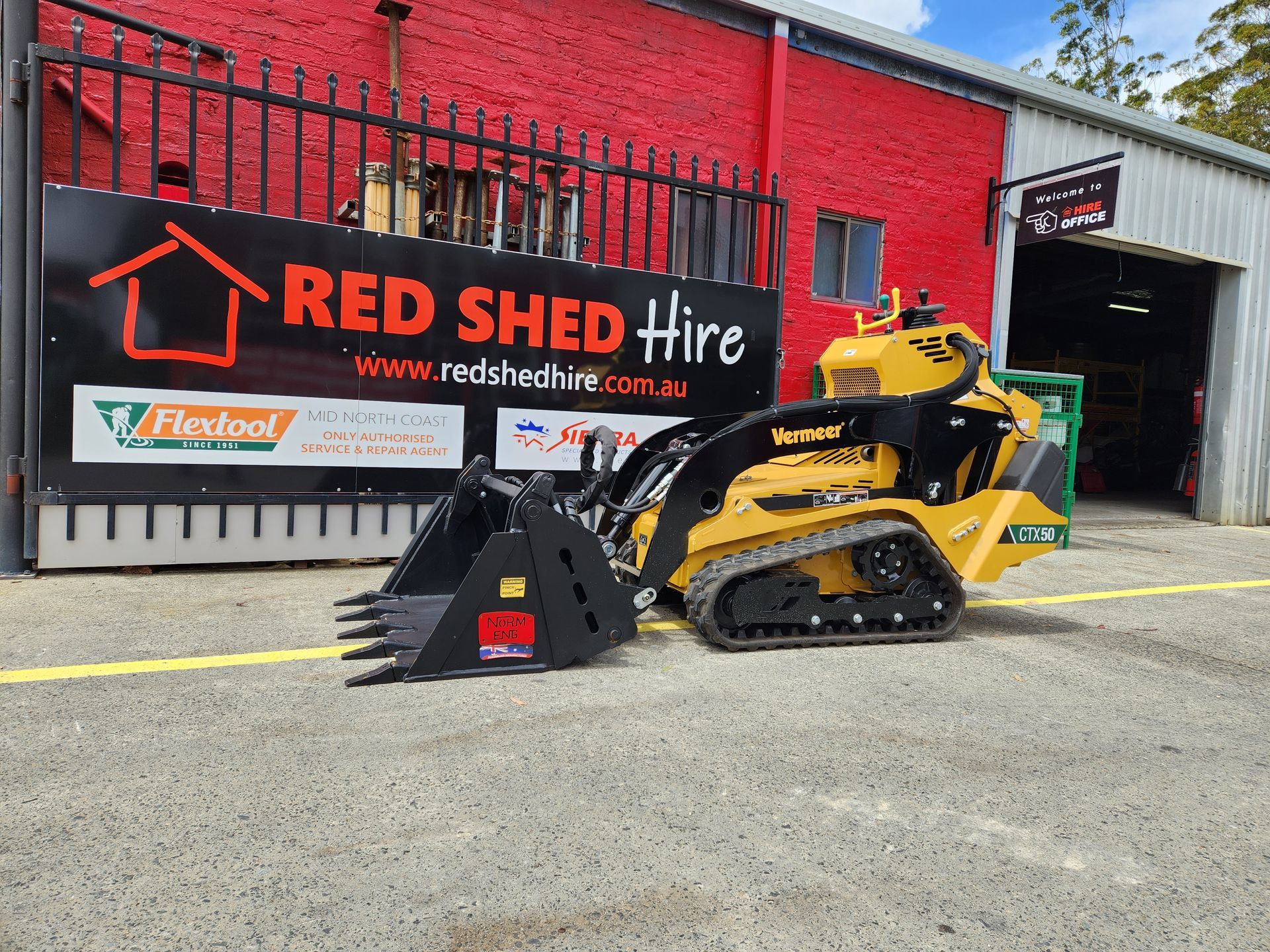 A Yellow Bulldozer Is Parked In Front Of A Red Shed Hire Sign — Red Shed Hire In Wauchope, NSW