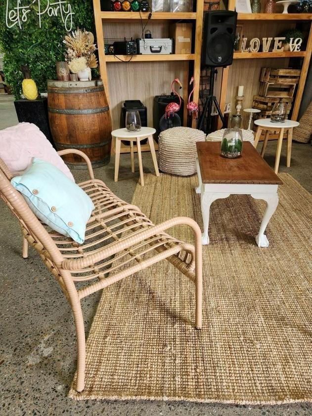 A Wicker Chair Is Sitting On A Rug Next To A Wooden Table — Red Shed Hire In Wauchope, NSW
