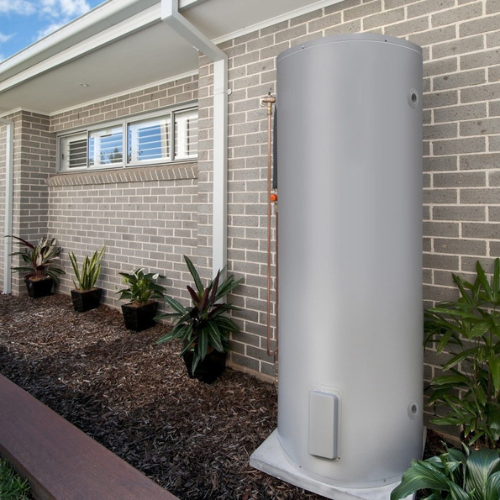 A White Water Heater is Sitting on the Side of a Brick Building — Coastwide Plumbing Solutions in Sippy Downs, QLD