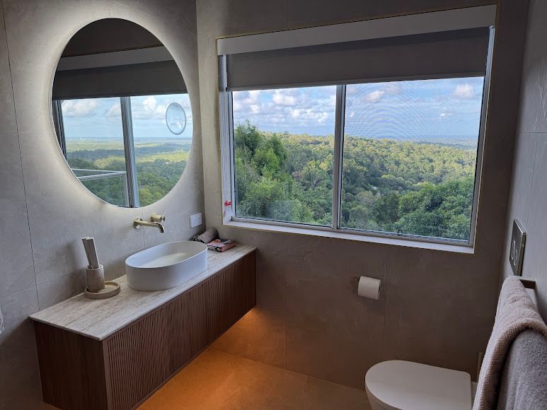A Bathroom With a Toilet, Sink, Mirror and Window — Coastwide Plumbing Solutions in Maroochydore, QLD