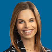 A smiling professional with light brown hair wearing a black-and-white grid pattern blazer against a blue background.