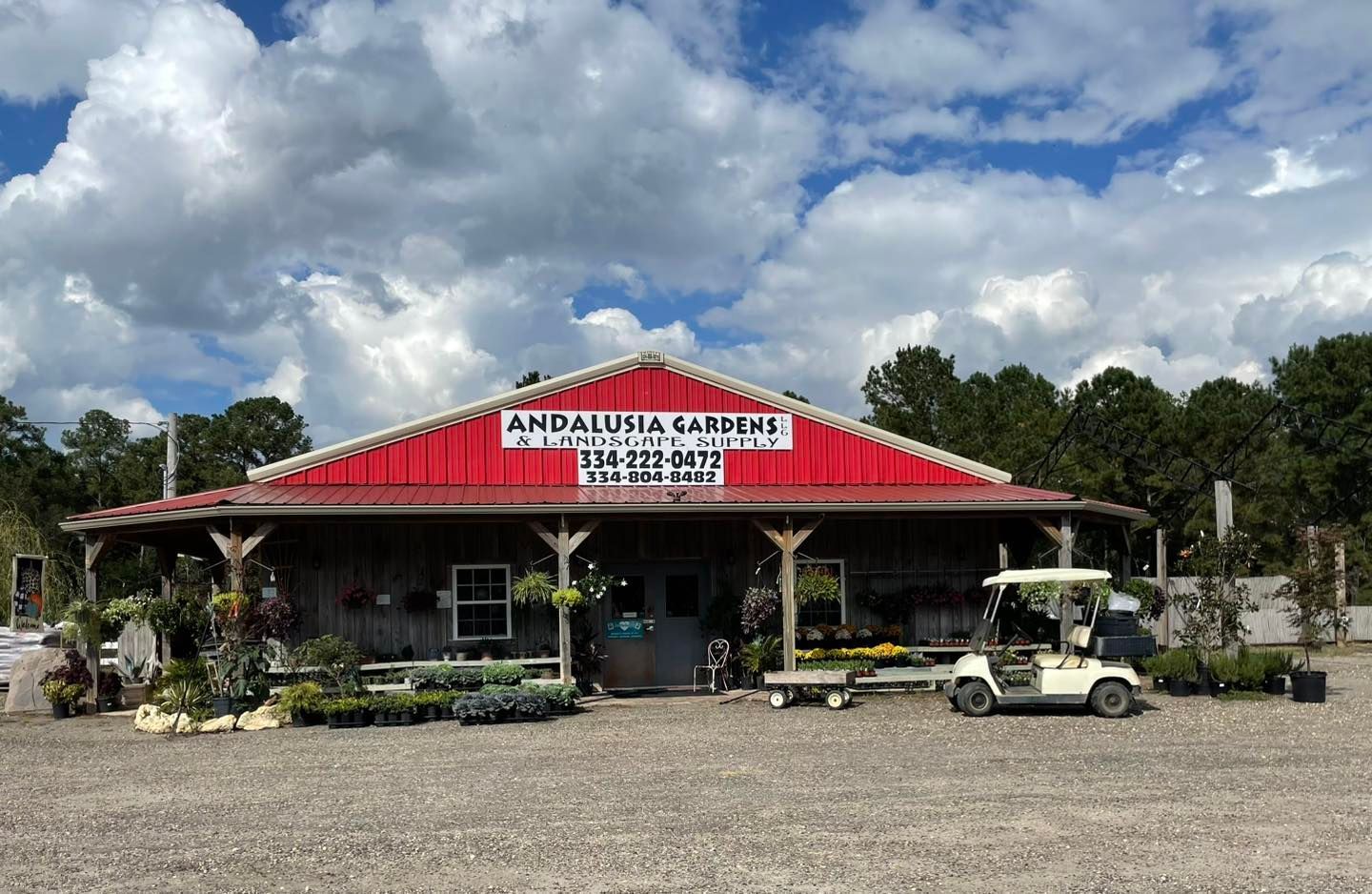 Andalusia Flowers and Gifts store with a red roof, a porch, and a golf cart on a gravel lot under a cloudy sky.