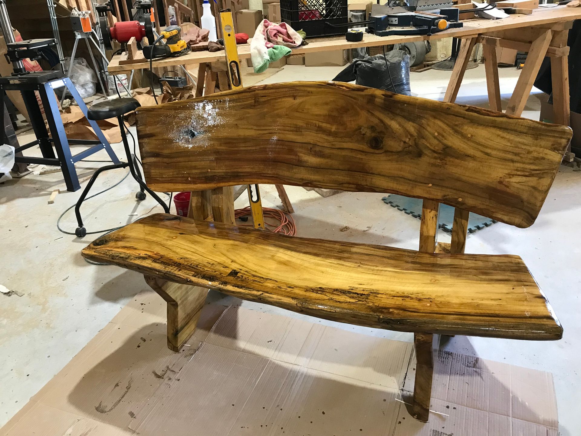 Wood slab bench in workshop, with natural edge back and seat, golden-toned finish.