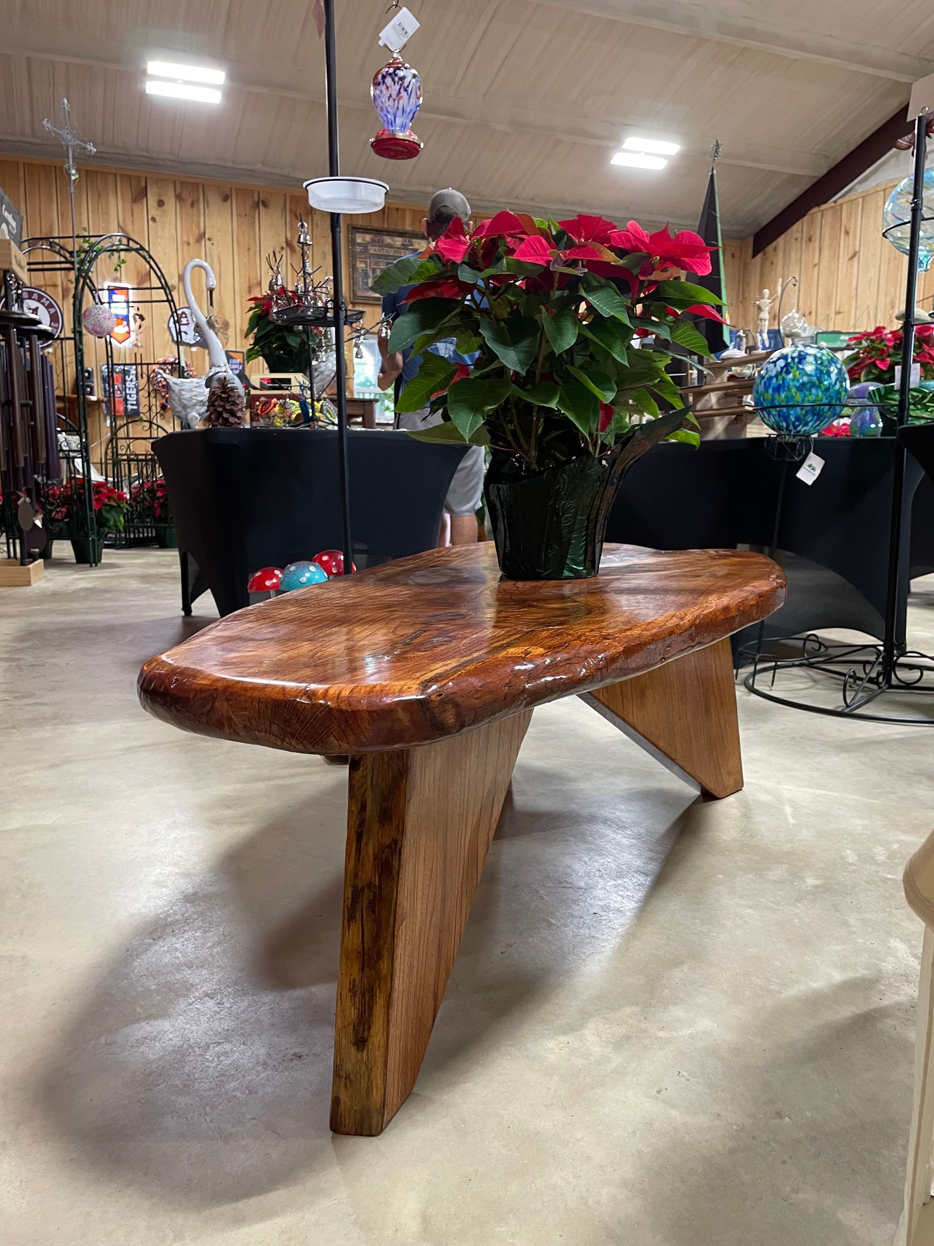 A wooden bench with a poinsettia in a green pot on top, inside a store.