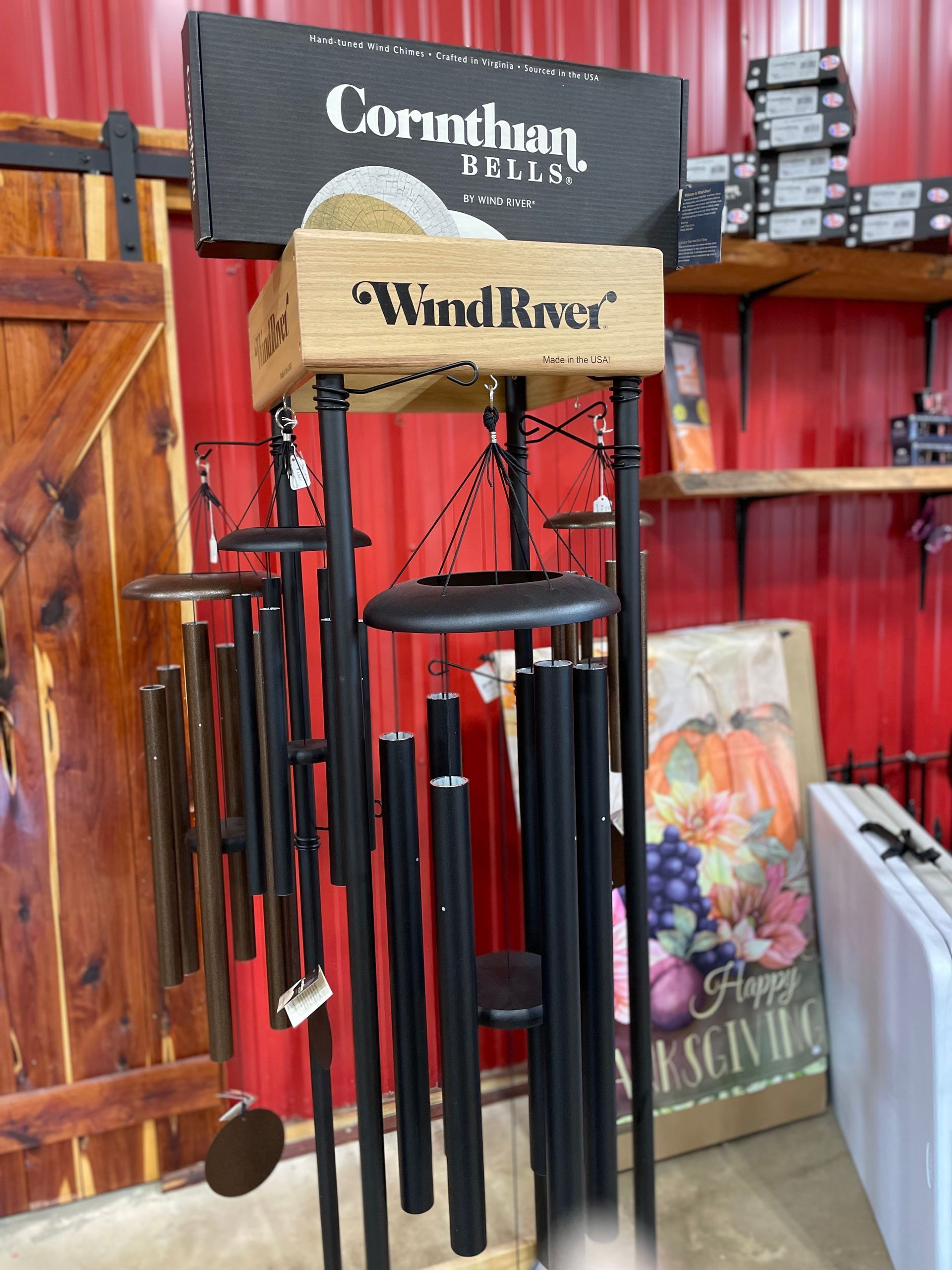 Wind chimes with black tubes and wooden top in a store setting, with a pumpkin and colorful sign in the background.