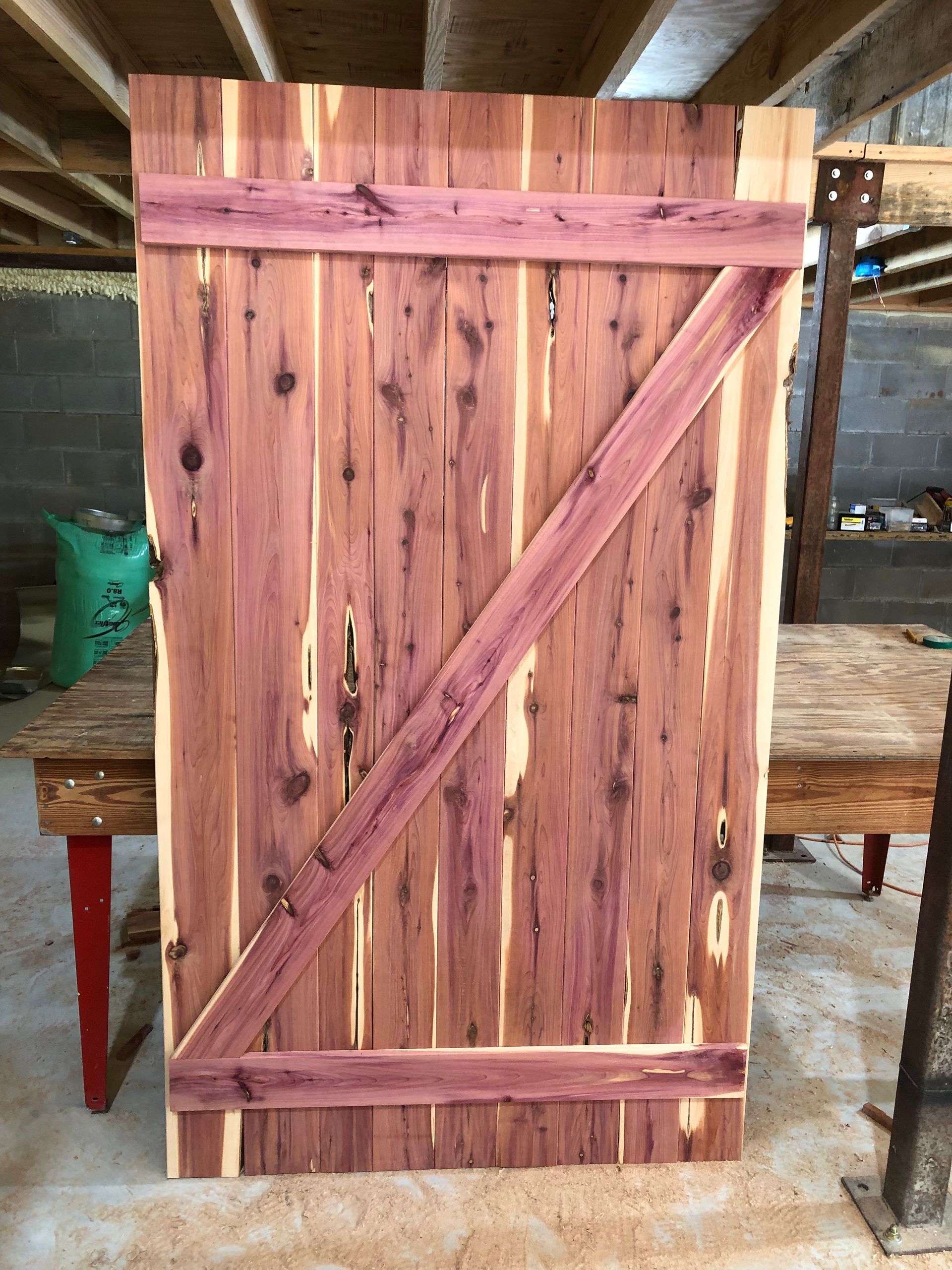 Cedar wood door with purple-toned support beams. Leaning against a table in a workshop setting.