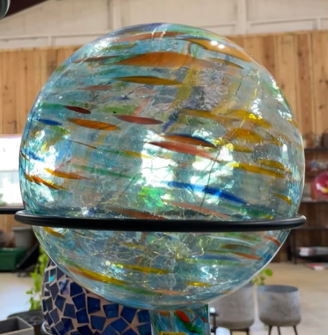 Glass gazing globe with blue, orange, and yellow streaks, displayed in a black ring stand.