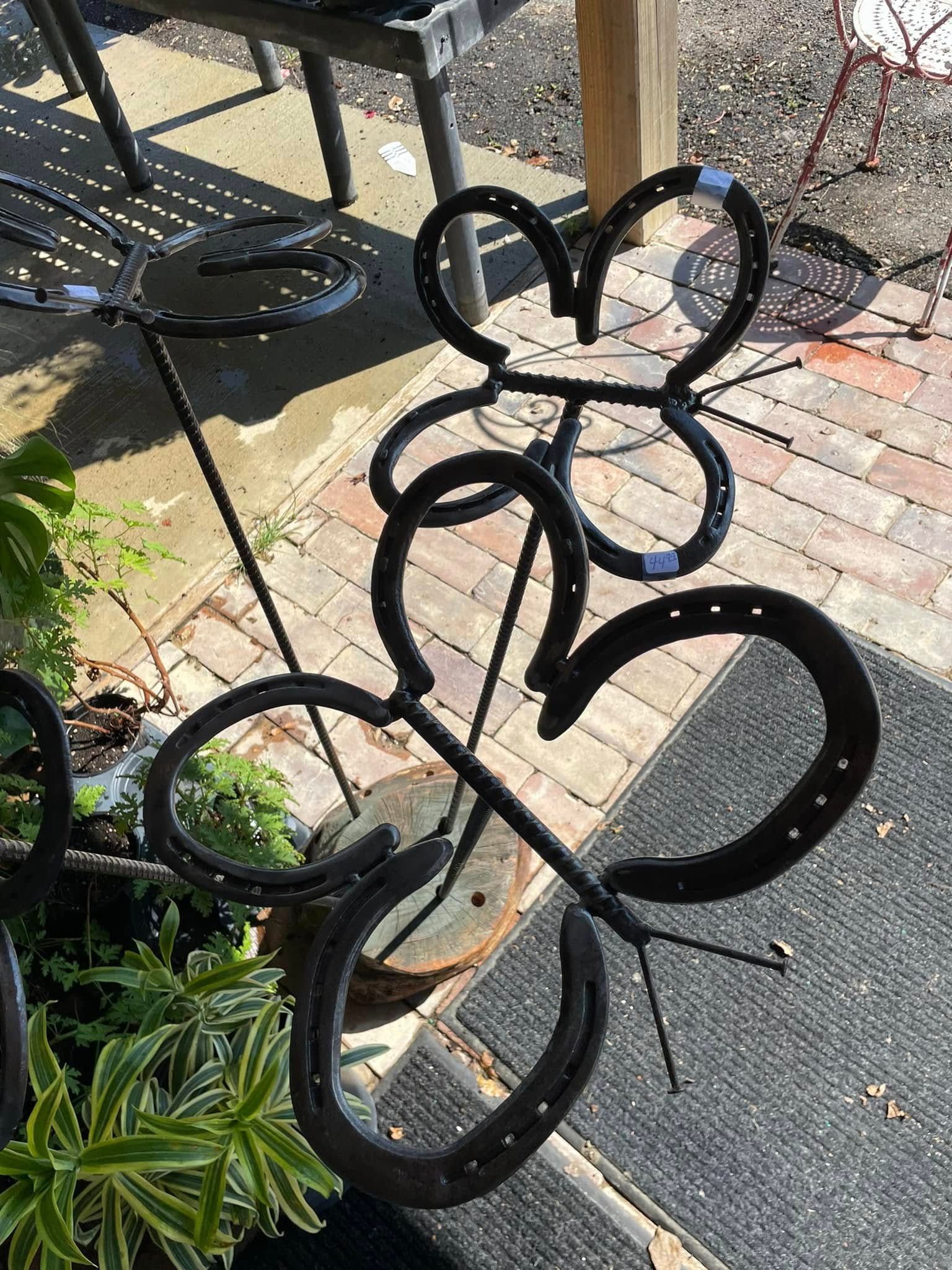 Black metal butterfly sculpture made of horseshoes on brick patio.
