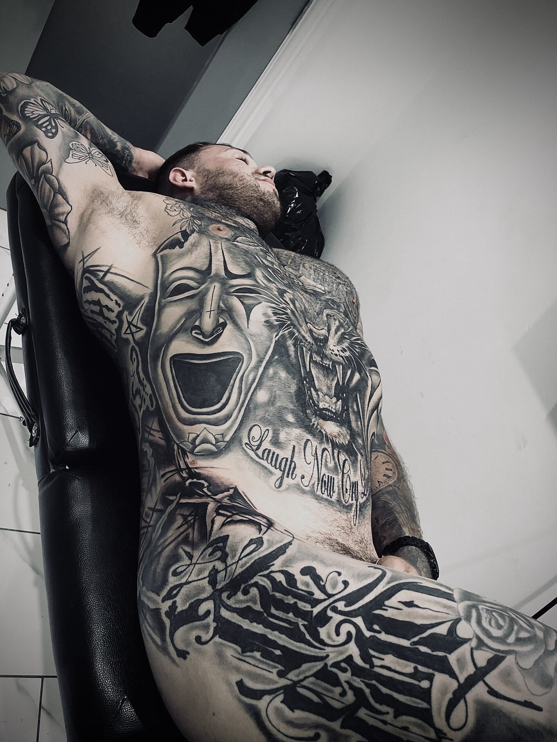 A man with a lot of tattoos on his body is laying on a chair.