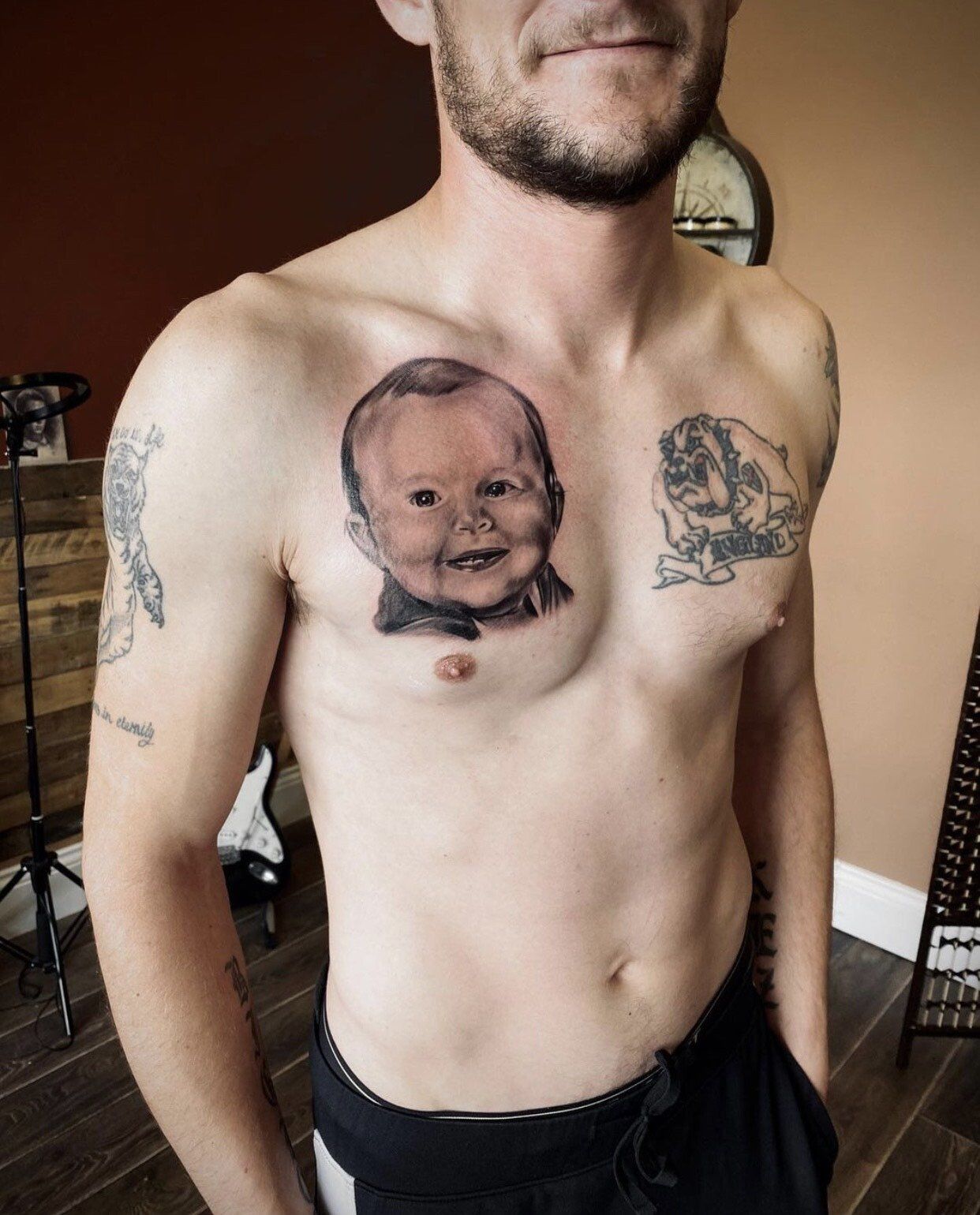 A shirtless man has a tattoo of a baby on his chest.