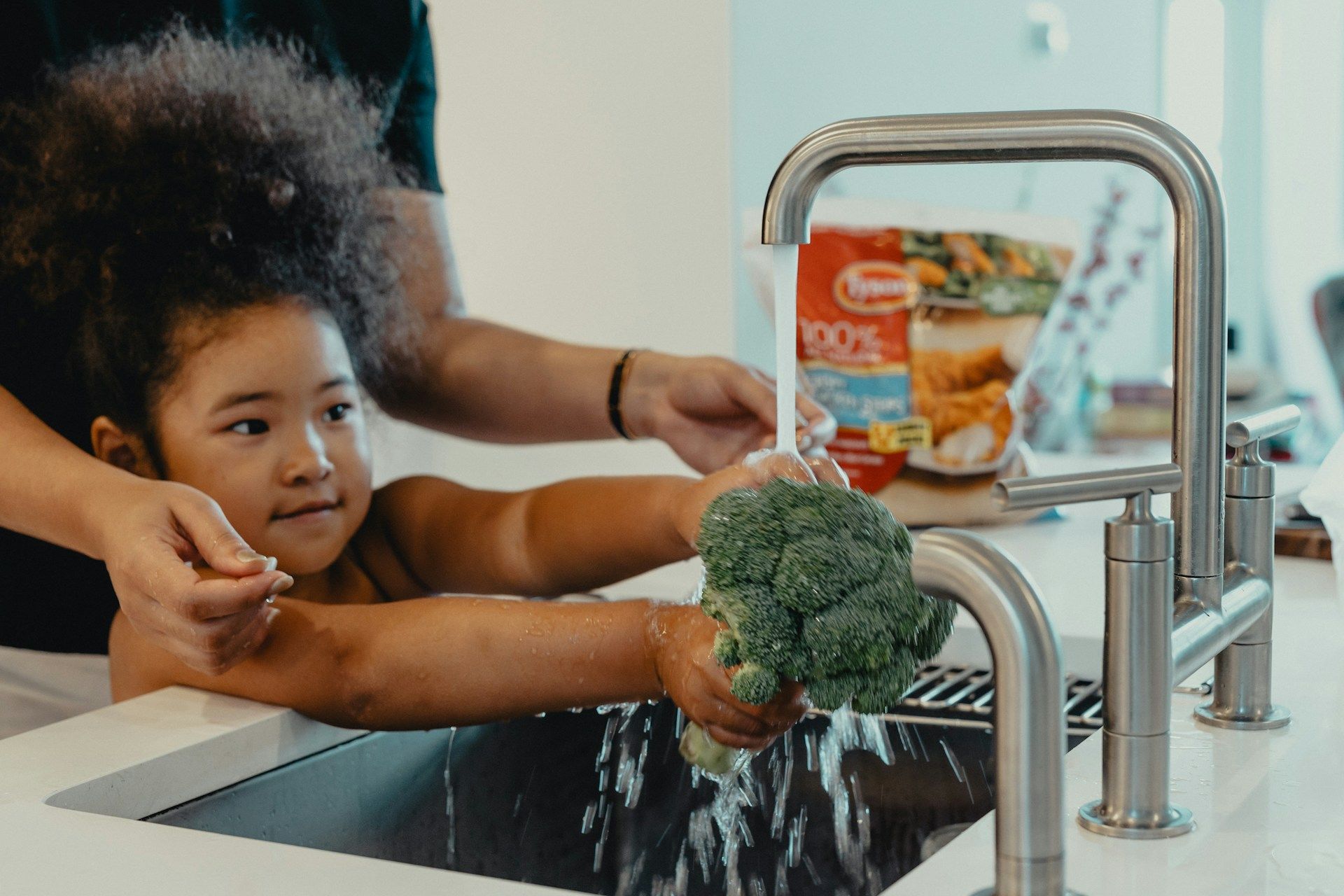 child washing broccoli in kitchen sink