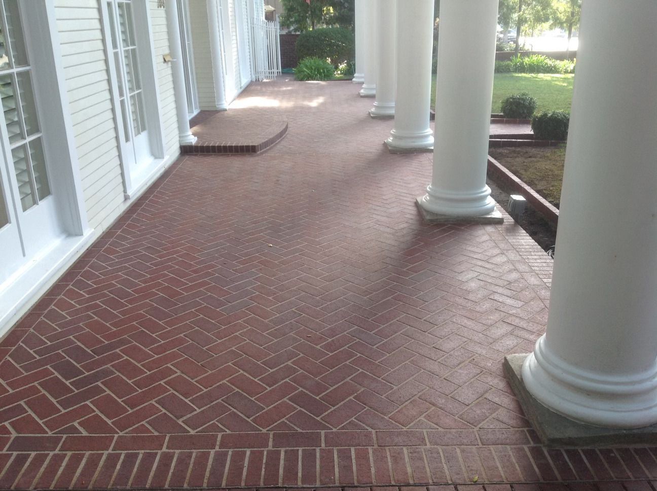 A brick porch with white columns and a herringbone pattern