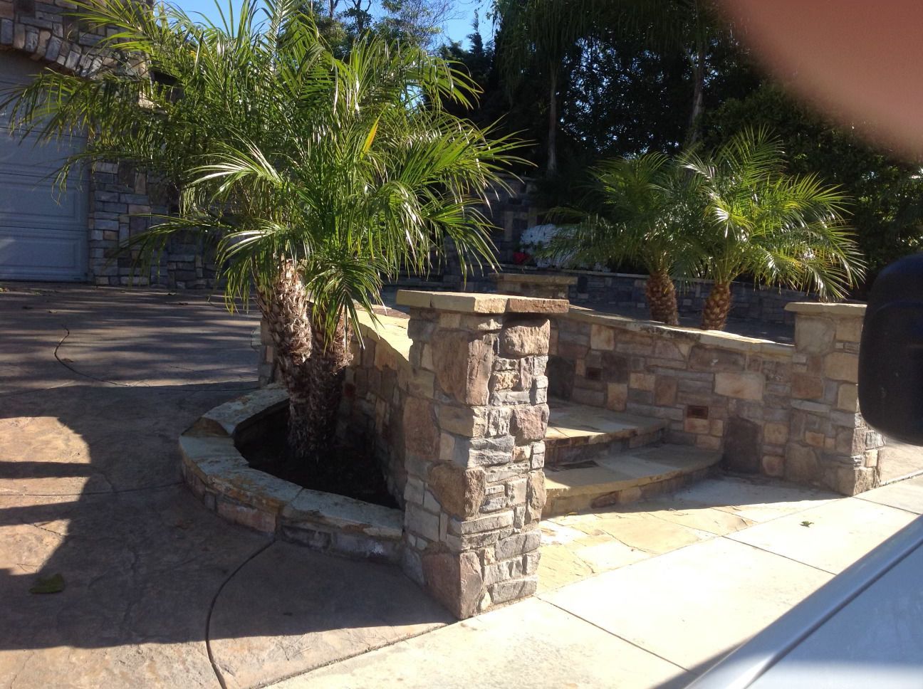 A stone wall with stairs and palm trees in front of a garage.