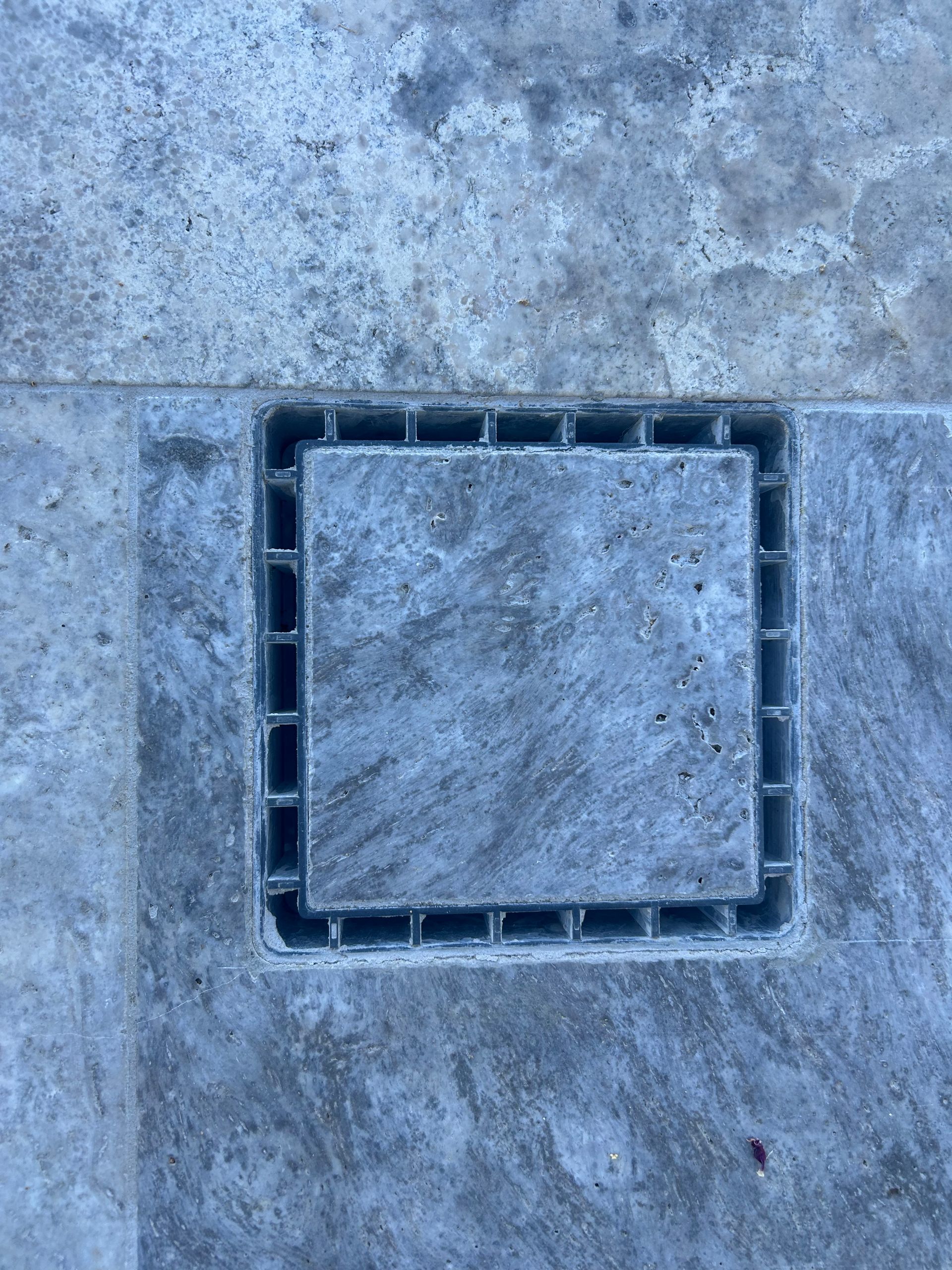 A close up of a square drain on a tiled floor.