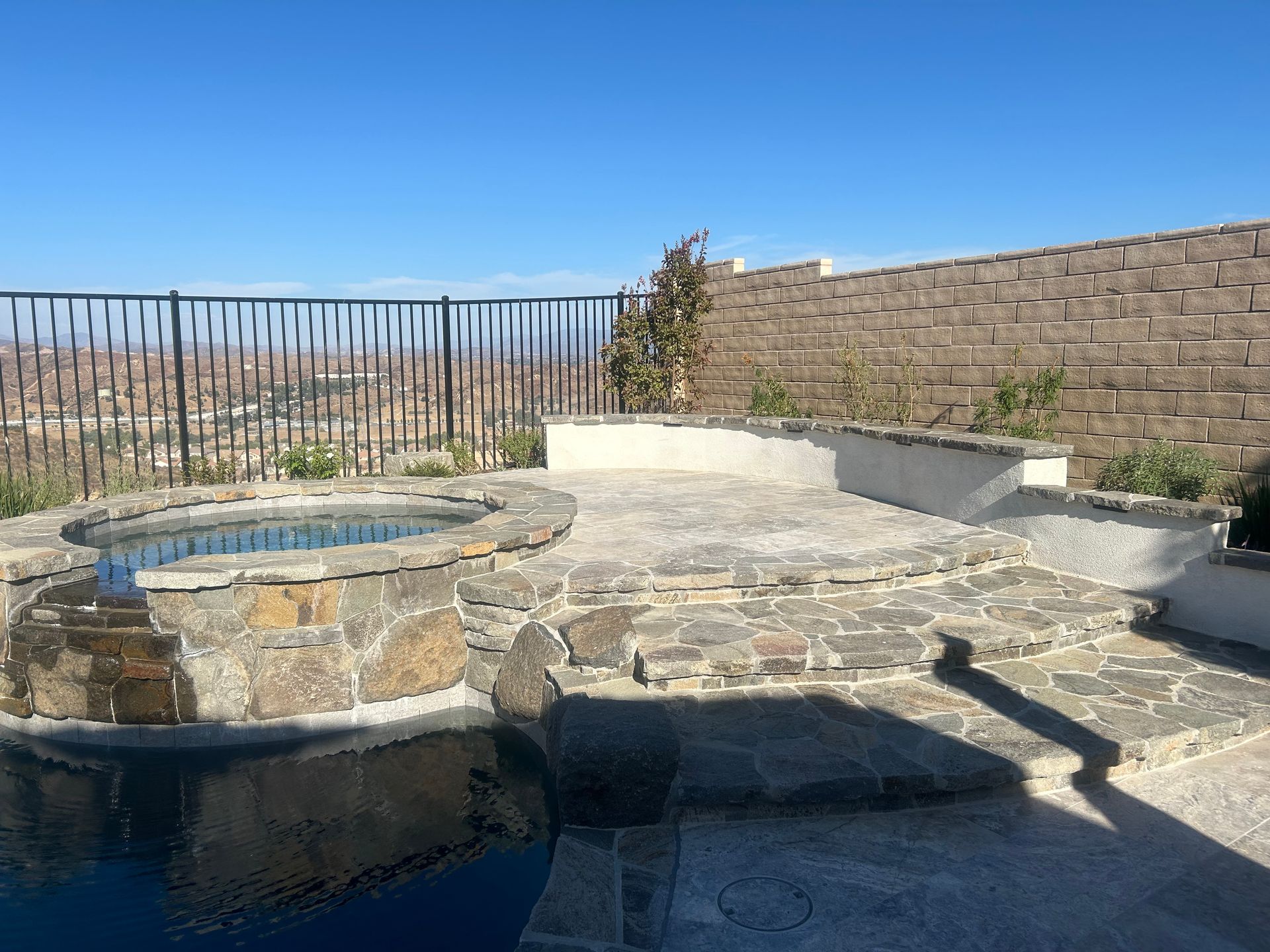 A patio with a hot tub and a brick wall.