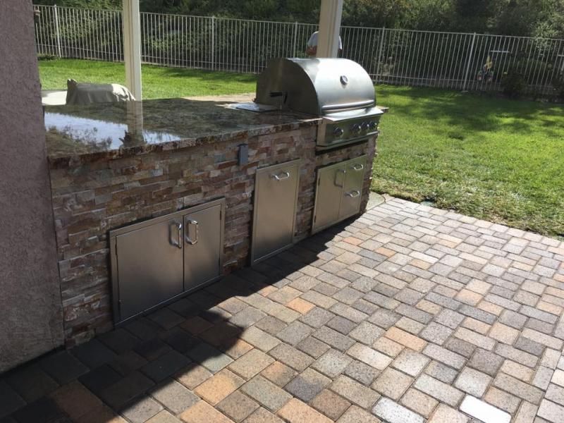 A grill is sitting on a brick patio next to a fence.