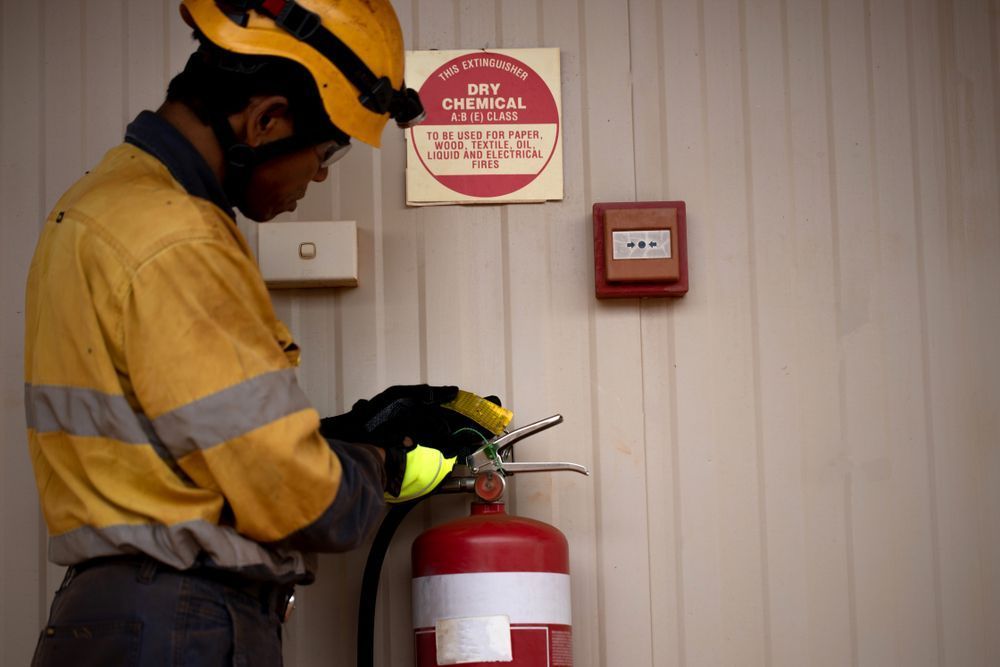 Man In Uniform Checking Fire Extinguisher — Fire Safety in Armidale, NSW