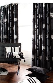 Black floral curtains frame a window. A black chair has white pillows and a blanket.