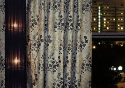 Floral patterned curtains partially covering a window with city lights visible at night.