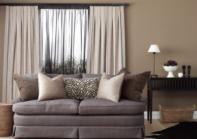 Gray couch with beige and zebra print pillows, sheer brown curtains, brown walls, and dark wood console.