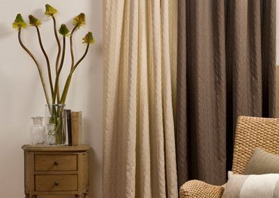 Nightstand with flowers and beige and brown curtains next to a wicker chair.