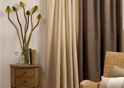 Nightstand with flowers, two-tone curtains (beige and brown), and wicker chair.