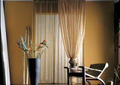 Room with sheer curtains, yellow walls, tall vase with flowers, and a chair.