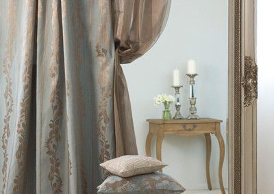 Curtains draped beside a mirror and small table with candles. Two pillows rest on the floor.