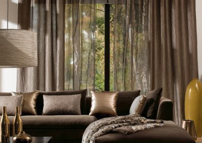Living room with brown sofa, pillows, and sheer curtains; a window with a forest view.