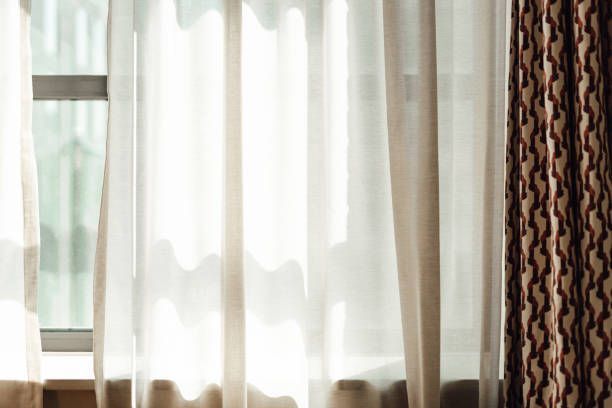 Window with sheer white curtains and patterned brown drapes, letting in sunlight.