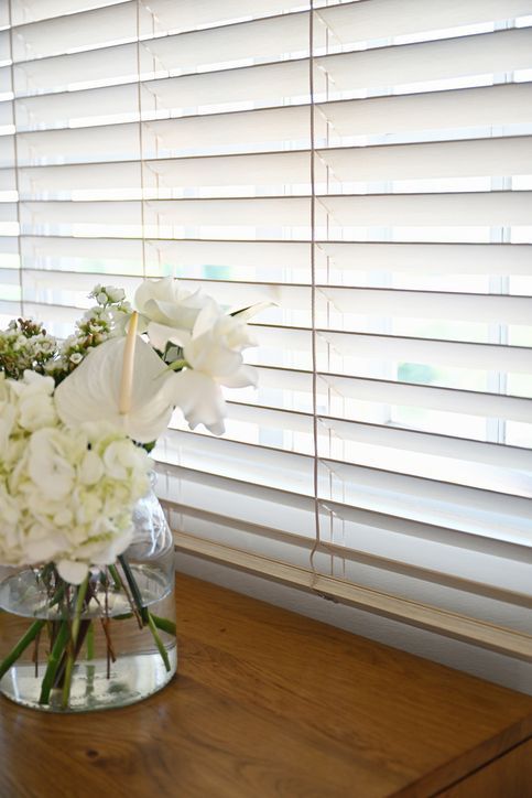 White blinds partially covering a window, set against a white wall.