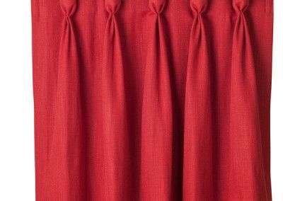 Red curtain with several pleats at the top, hanging vertically against a white background.