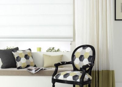 A black chair with geometric patterned upholstery sits near a window with white curtains.