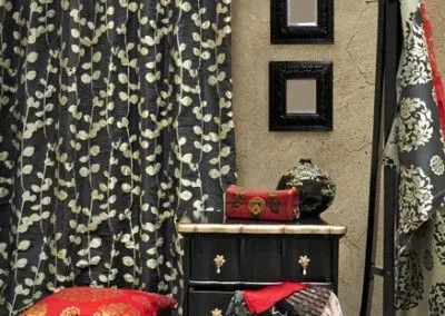 Black and gold patterned curtains frame a black nightstand with red accents, decorative vases, and framed mirrors.