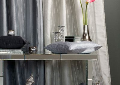 Mirrored console table with decorative pillows, candles, vase with flower, and gray and white curtains.
