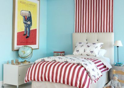 Bedroom with a blue wall, red and white striped bedding, artwork, and a bedside table.