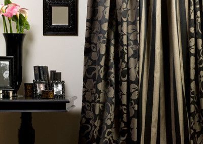 Black and beige floral curtains beside striped curtain. A black table with decor and flowers.