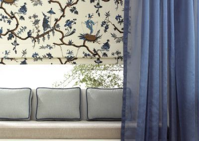 Window seat with patterned blind, blue curtain, and three pillows.